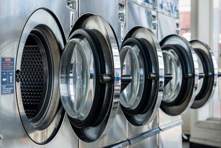 A row of commercial self-service washing machines with their doors open